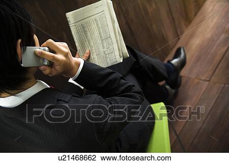 Businessman talking on a mobile phone while looking at a newspaper View Large Photo Image Stock Image - Businessman talking on a mobile phone while looking at a newspaper. Fotosearch