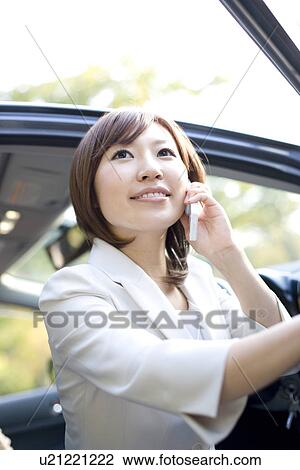 Stock Image - Businesswoman getting out of car and talking on mobile phone. Fotosearch
