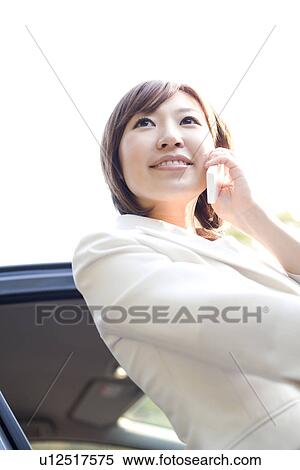 Stock Photography - Businesswoman getting out of car and talking on mobile phone. Fotosearch