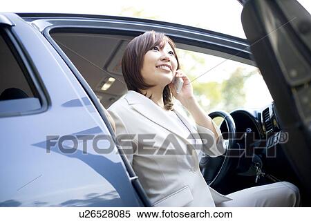 Stock Photography - Businesswoman getting out of car and talking on mobile phone. Fotosearch
