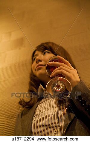 Picture - Businesswoman leaning against a wall with a glass of wine. Fotosearch