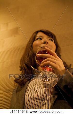 Stock Image - Businesswoman leaning against a wall with a glass of wine. Fotosearch