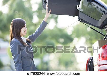 Picture - Businesswoman loading cardboard boxes into car. Fotosearch