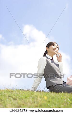 Stock Image - Businesswoman sitting on grass and using mobile phone. Fotosearch
