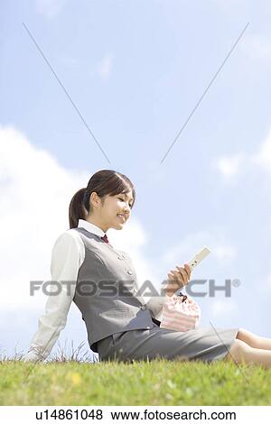 Stock Photo - Businesswoman sitting on grass and using mobile phone. Fotosearch
