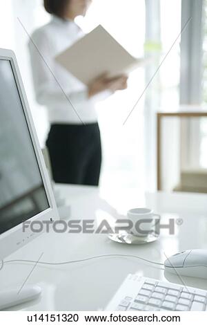 Stock Image - Businesswoman standing near computer desk. Fotosearch