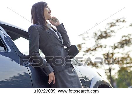 Stock Photo - Businesswoman standing next to car talking on mobile phone. Fotosearch