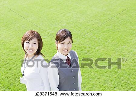 Stock Photo - Businesswomen standing on green grass, smiling at the camera. Fotosearch