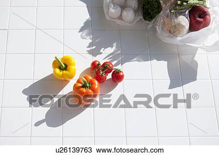 Stock Image - Capsicums and tomatoes next to plastic shopping bags containing more groceries. Fotosearch