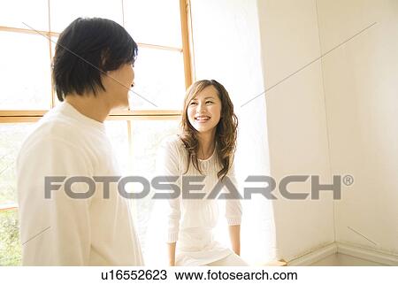 Stock Image - Cheerful woman and man talking near window. Fotosearch