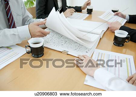 Stock Image - Colleagues working at desk in office with blueprints. Fotosearch