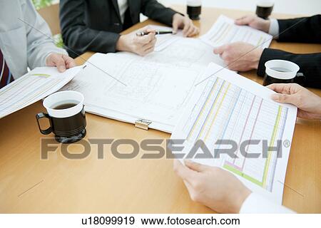 Stock Photo - Colleagues working at desk in office with blueprints. Fotosearch