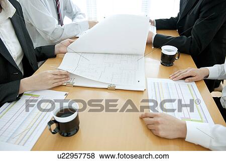 Colleagues working at desk in office with blueprints View Large Photo Image Stock Photo - Colleagues working at desk in office with blueprints. Fotosearch