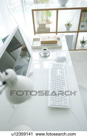 Stock Image - Computer on desk in room with bookshelf. Fotosearch