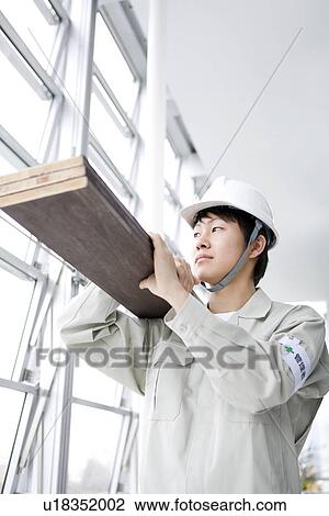 Stock Image - Construction worker carrying wooden planks. Fotosearch