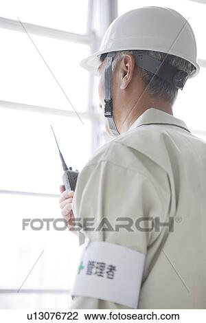 Stock Image - Construction worker holding walkie-talkie. Fotosearch