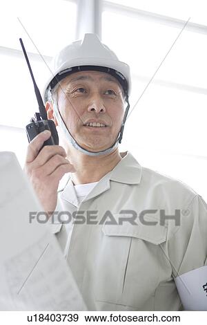 Stock Photo - Construction worker holding walkie-talkie and blueprint. Fotosearch