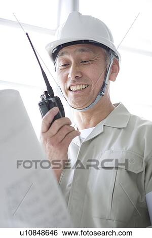 Stock Photograph - Construction worker holding walkie-talkie and blueprint. Fotosearch