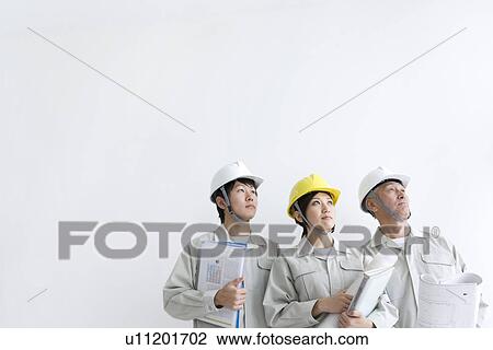 Stock Image - Construction workers holding blueprints and documents. Fotosearch