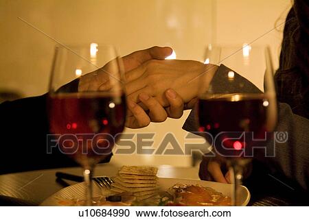 Stock Image - Couple holding hands over a table. Fotosearch