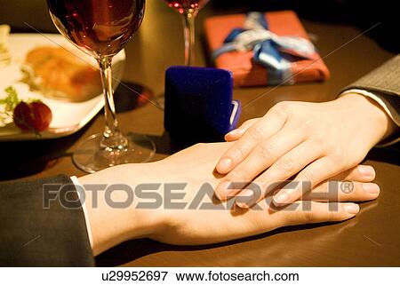 Stock Photo - Couple holding hands with a jewelry box on the table. Fotosearch