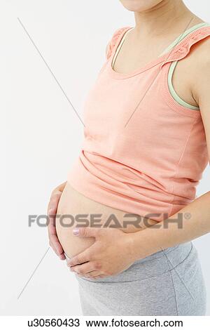 Stock Image - Cropped image of a pregnant woman with her hands on her stomach. Fotosearch