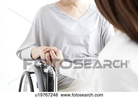 Stock Photo - Daughter holding the hand of her mother in a wheelchair. Fotosearch