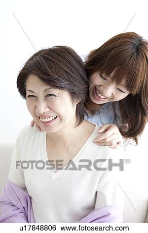 Stock Photograph - Daughter standing behind her mother and laughing. Fotosearch