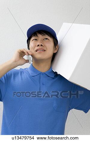 Delivery man holding package and talking on cellphone View Large Photo Image Picture - Delivery man holding package and talking on cellphone. Fotosearch