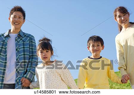 Stock Image - Family of four holding hands against a blue sky. Fotosearch