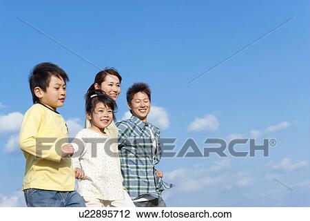 Stock Image - Family of four holding hands against a blue sky. Fotosearch