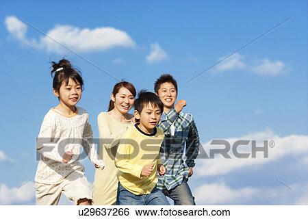 Stock Photograph - Family of four running against a blue sky. Fotosearch