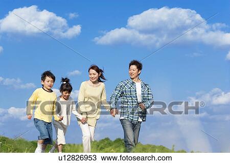 Family of four running and holding hands at the park against a blue sky View Large Photo Image Stock Image - Family of four running and holding hands at the park against a blue sky. Fotosearch