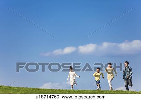 Stock Image - Family of four running at the park against a blue sky. Fotosearch