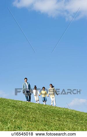 Stock Photo - Family of four walking and holding hands at the park against a blue sky. Fotosearch