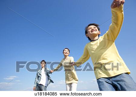 Stock Photography - Family with young son holding hands against a blue sky. Fotosearch