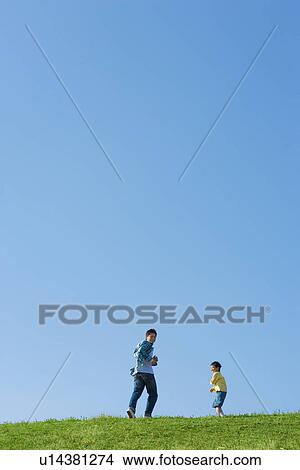 Picture - Father and son running up a hill against a clear blue sky. Fotosearch