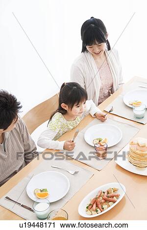 Stock Image - Father, mother and daughter sitting at breakfast table together. Fotosearch