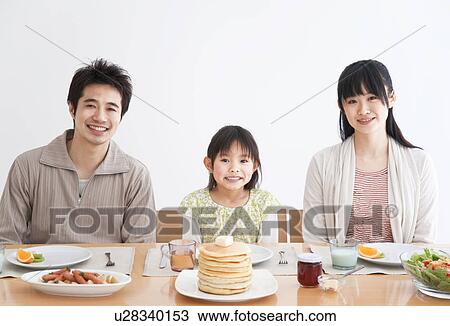 Stock Image - Father, mother and daughter sitting at breakfast table together. Fotosearch