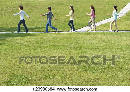 Picture - Five people walking on footpath near grass. Fotosearch
