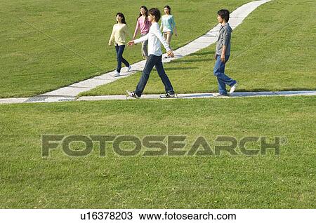 Stock Image - Five people walking on footpath near grass. Fotosearch