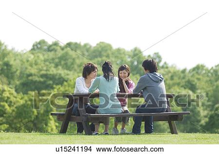 Four people sitting together at picnic table View Large Photo Image Picture - Four people sitting together at picnic table. Fotosearch