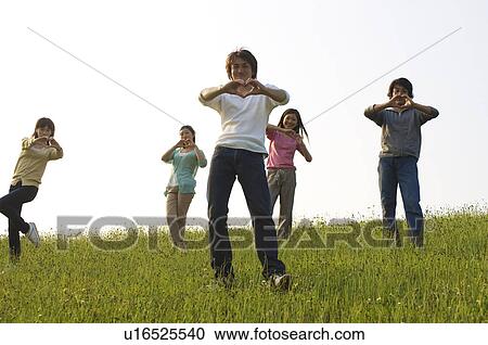 Stock Image - Friends making heart shapes with their hands in a field. Fotosearch