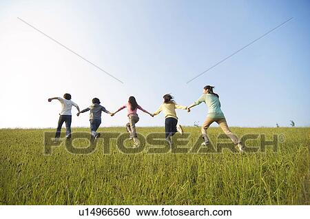 Friends running hand in hand through a field View Large Photo Image Stock Image - Friends running hand in hand through a field. Fotosearch