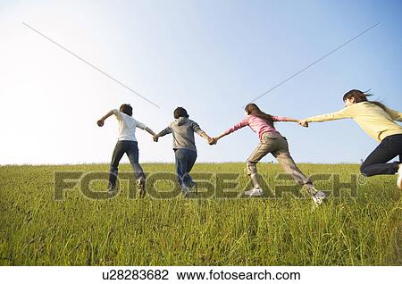Friends running hand in hand through a field View Large Photo Image Stock Image - Friends running hand in hand through a field. Fotosearch