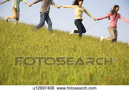 Friends running hand in hand through a field View Large Photo Image Stock Photo - Friends running hand in hand through a field. Fotosearch