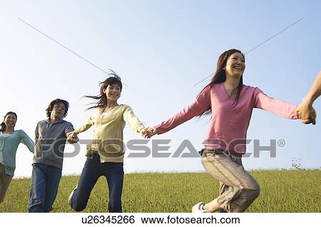 Friends running hand in hand through a field View Large Photo Image Stock Photograph - Friends running hand in hand through a field. Fotosearch