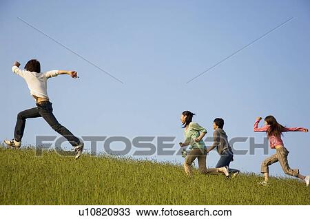 Stock Image - Friends running up a grassy hill. Fotosearch