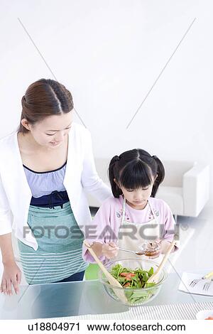 Stock Image - Girl adding salad dressing to salad with her mother. Fotosearch