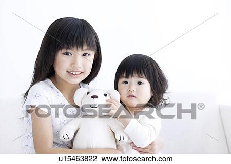 Stock Image - Girl holding her baby sister and a teddy bear. Fotosearch
